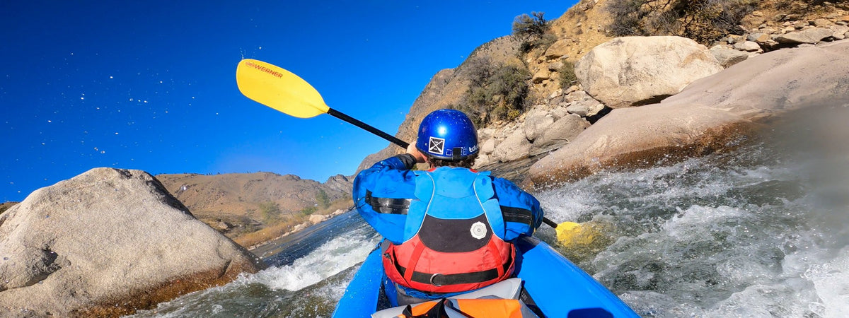 Paddler in a blue AIRE inflatable kayak running a whitewater rapid in a granite canyon